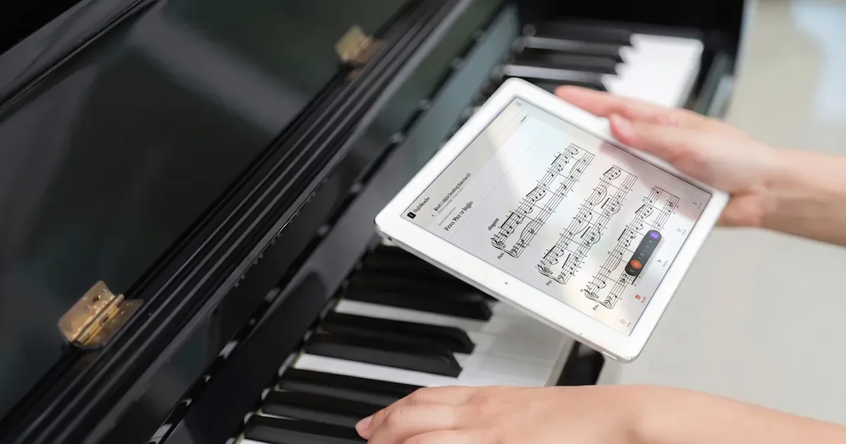 A pianist practising at a keyboard while consulting a tablet